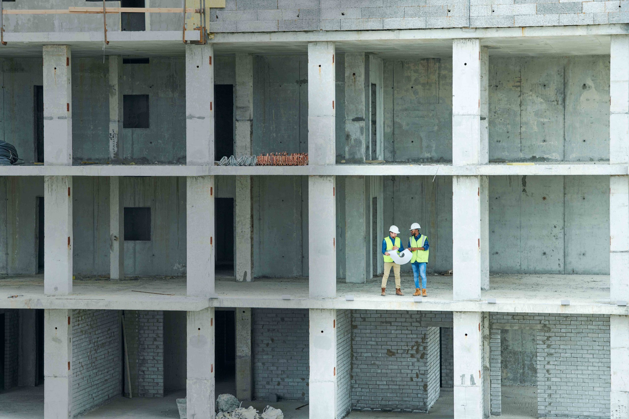 Two men with draft standing on floor of unfinished building on construction site